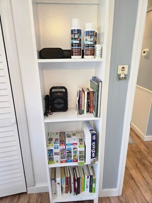 A bookshelf with various items including books, a camera, and cleaning products. - Barking Bayside Bungalow (Lower Township)