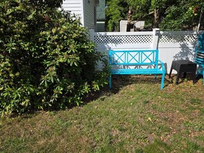 A backyard with a blue bench, a white fence, and a bush. - Barking Bayside Bungalow (Lower Township)