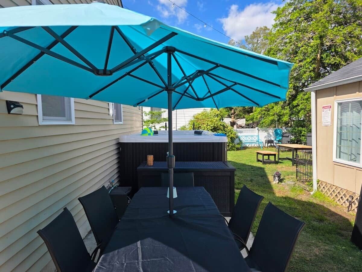 An outdoor patio with a table and chairs, a large umbrella, and a hot tub in the background.