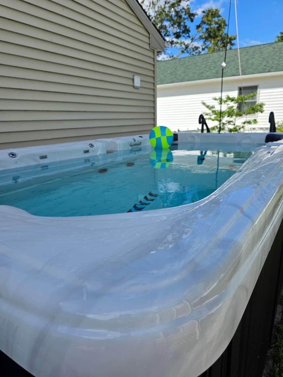 Ein Whirlpool mit einer klaren Kunststoffabdeckung, einem blauen und grünen Ball und einem Haus im Hintergrund.