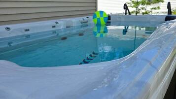 Ein Whirlpool mit einer klaren Kunststoffabdeckung, einem blauen und grünen Ball und einem Haus im Hintergrund.