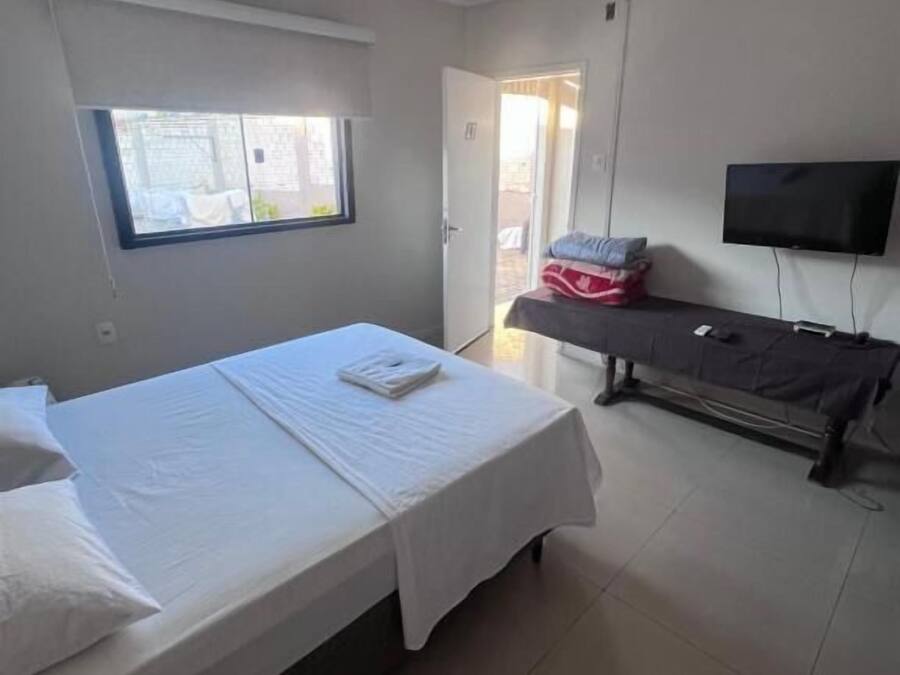 Un dormitorio con cama, televisor montado en la pared y ventana.