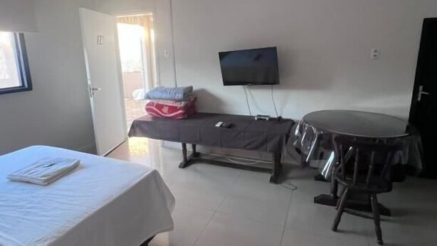 A room with a bed, a television, a table, and a door leading to another room. - CITY HOTEL IJUÍ (Ijuí)