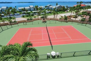 Cancha de tenis con una red, rodeada de palmeras y vista al océano.