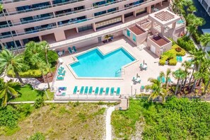 Eine Vogelperspektive auf ein Hotel mit einem zentralen Schwimmbecken, mehreren Liegebereichen und umgebender Bepflanzung.