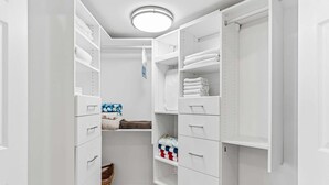 Ein begehbarer Kleiderschrank mit weißen Regalen, Schubladen und einer blauen Mülltonne.