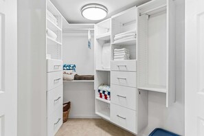 Ein begehbarer Kleiderschrank mit weißen Regalen, Schubladen und einer blauen Mülltonne.