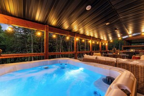 A hot tub area with a wooden deck, wicker furniture, and string lights.