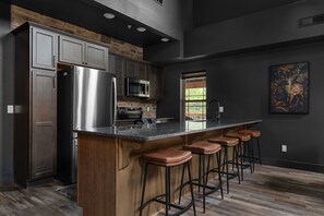 Una cocina moderna con electrodomésticos de acero inoxidable, una zona de bar con taburetes y un amplio ventanal.