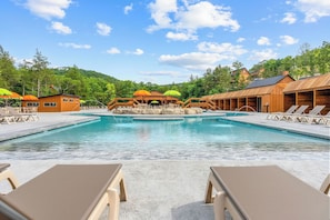 A pool area with lounge chairs and umbrellas, surrounded by wooden buildings and trees.