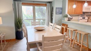 A dining area with a large table, chairs, a bowl, and a view of the outside. - OBXcitement: Oceanfront Condo, Water Views, Community Pool and Tennis Courts (Nags Head)