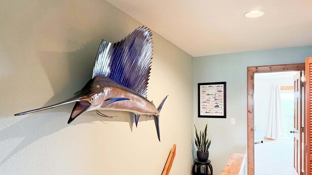 A mounted fish on the wall, a framed fish illustration, a potted plant, and a wooden bench. - OBXcitement: Oceanfront Condo, Water Views, Community Pool and Tennis Courts (Nags Head)