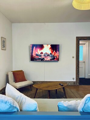 Ein Wohnzimmer mit einem an der Wand befestigten Flachbildfernseher, einer Couch mit Kissen, einem Holztisch und einer Tür zu einem anderen Raum.