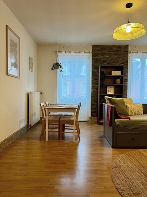 Ein Wohnzimmer mit Esstisch, Sofa, einer Pendelleuchte und einem Bücherregal.