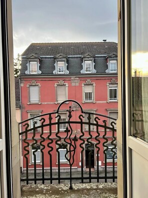 A balcony with a wrought iron railing, a red building with multiple windows, and a tiled roof. - T2 cocooning à 10min à pied du Centre de Colmar (Colmar)