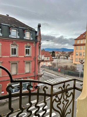 En balkong med utsikt över en gata och byggnader, inklusive en röd byggnad med en balkong och en skylt med texten ”Saint-Joseph”.