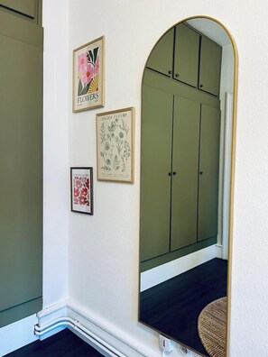 Ein Flur mit einer spiegelnden Schiebetür zum Kleiderschrank, gerahmten Pflanzenbildern und einem kleinen Teppich.