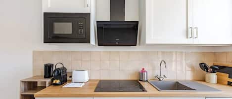 A modern kitchen with white cabinets, a black microwave, a built-in oven, a stainless steel sink, and a wooden countertop.
