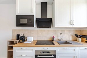 Eine moderne Küche mit weißen Schränken, einer schwarzen Mikrowelle, einem eingebauten Backofen, einer Edelstahl-Spüle und einer Holzausziehtafel.