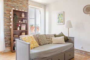 Un salon chaleureux avec un canapé gris, une bibliothèque en bois et une fenêtre donnant sur des immeubles.