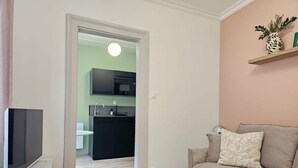 A living room with a flat-screen TV, a sofa with cushions, and a kitchen in the background. - Studio cocooning à 5km du centre de Strasbourg (Schiltigheim)