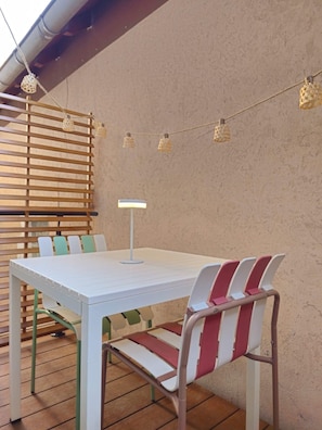 An outdoor patio with a white table, striped chairs, a lamp, and string lights. - Studio cocooning à 5km du centre de Strasbourg (Schiltigheim)
