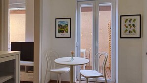 A room with a white round table, two white chairs, a television, and a door leading to an outdoor area. - Studio cocooning à 5km du centre de Strasbourg (Schiltigheim)