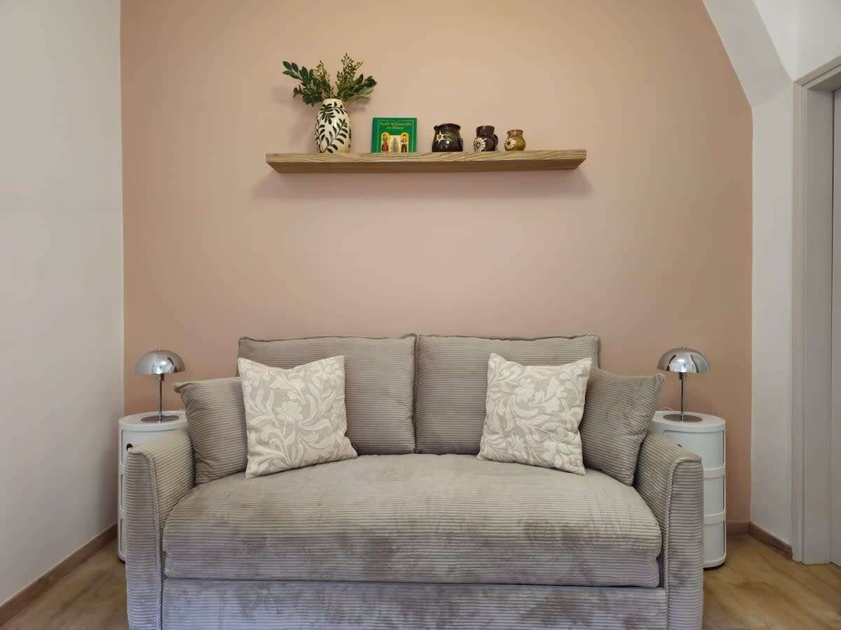 Ein Zimmer mit einer Couch, zwei Beistelltischen, einem Regal mit Dekoration und einer Tür.