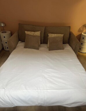 Ein Bett mit weißer Matratze und braunem Kopfteil, das von zwei Nachttischen mit Schubladen gesäumt wird.