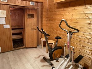 Ein Holzinnenraum mit Sauna, einer Holzbank und einem Crosstrainer.