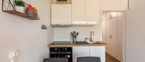 A compact kitchen with white cabinets, a black countertop, and a small dining area with two chairs.