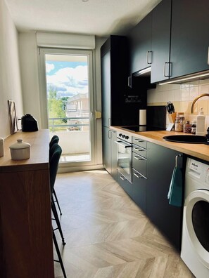 A modern kitchen with a large window, a dining area, and a washing machine. - T2 cosy idéalement placé à proximité du Zénith (Strasbourg)