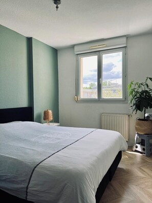 Ein Schlafzimmer mit einem Bett, einem Fenster, einer Heizung und einer Pflanze.