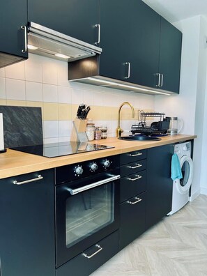 Eine moderne Küche mit schwarzen Schränken, einer Holz Arbeitsplatte, einem eingebauten Ofen und einer Waschmaschine.