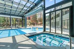 Ein Hallenbad mit klaren Glaswänden, einem Sprungturm und Liegestühlen.