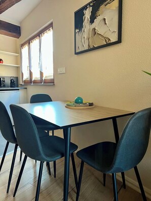 Ein Essbereich mit Tisch und Stühlen, einem Gemälde an der Wand und einem Fenster mit Vorhängen.