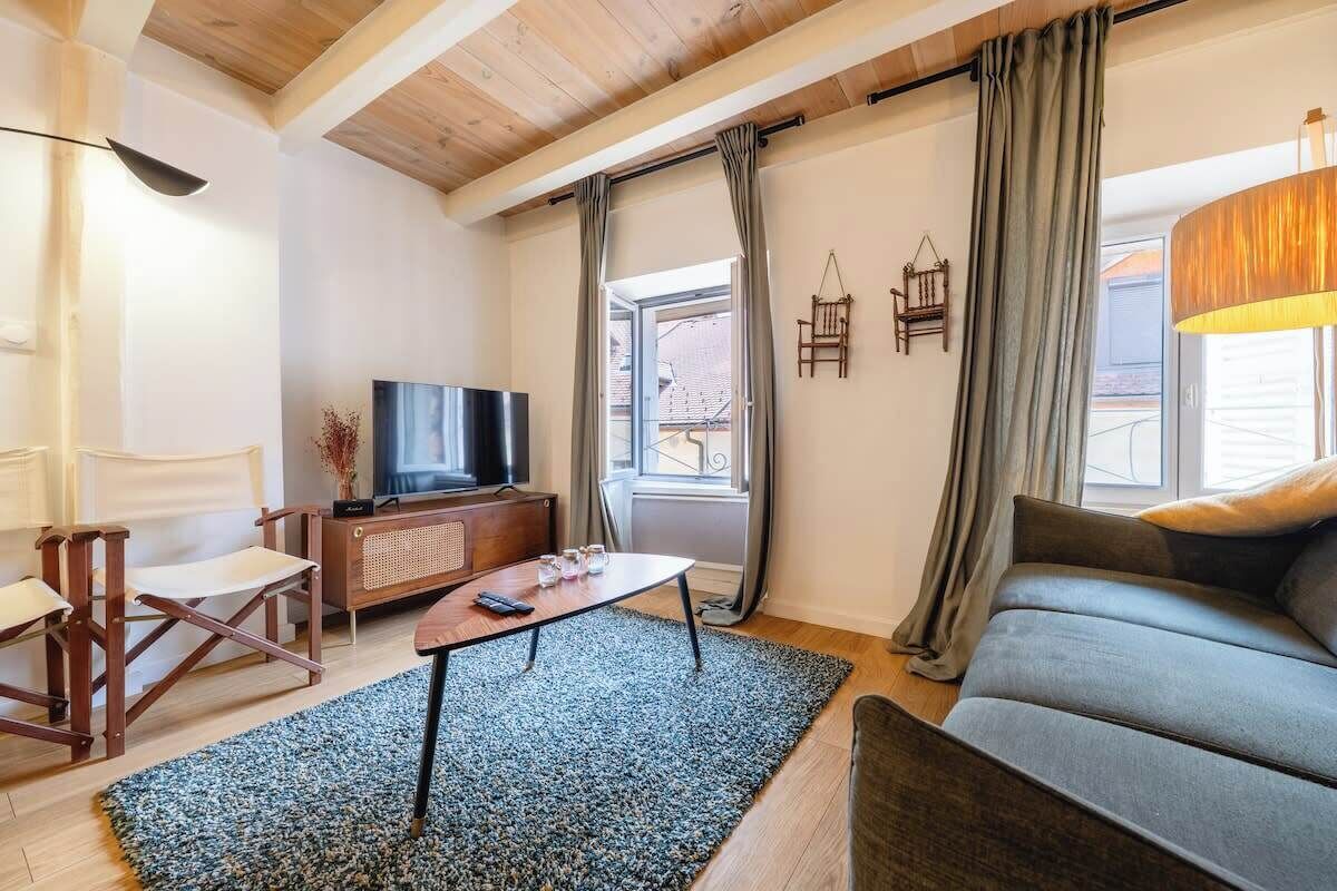 A living room with a sofa, a coffee table, a TV, and a window with curtains.