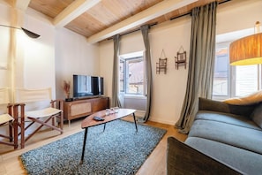 A living room with a sofa, a coffee table, a TV, and a window with curtains.