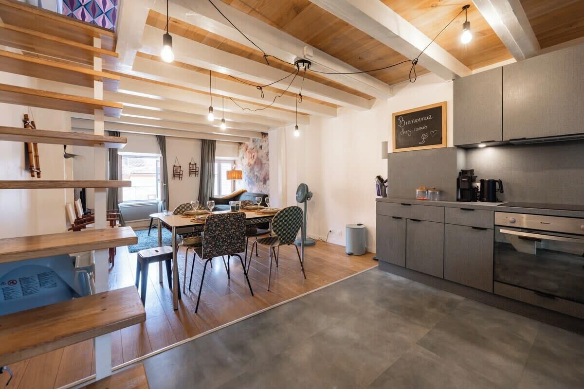 A modern kitchen with a dining area, wooden beams on the ceiling, and a chalkboard with a message.
