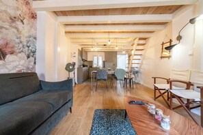 A living room with a sofa, a dining area with chairs, a kitchen in the background, wooden beams on the ceiling, and a wall with a floral mural. - Beautiful apartment in the heart of Annecy (Annecy)
