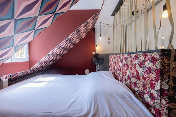 A room with a bed, a patterned wall, and a fan.