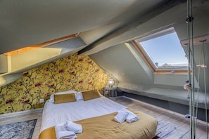 A bedroom with a sloped ceiling, a bed with white linens, a floral wallpaper, and a skylight. - Beautiful apartment in the heart of Annecy (Annecy)