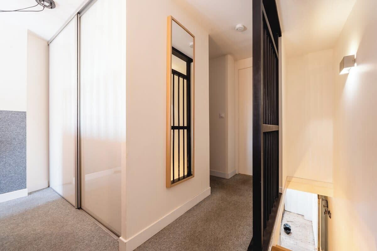 A hallway with a sliding door, a framed window with a black grille, and a light fixture on the wall.