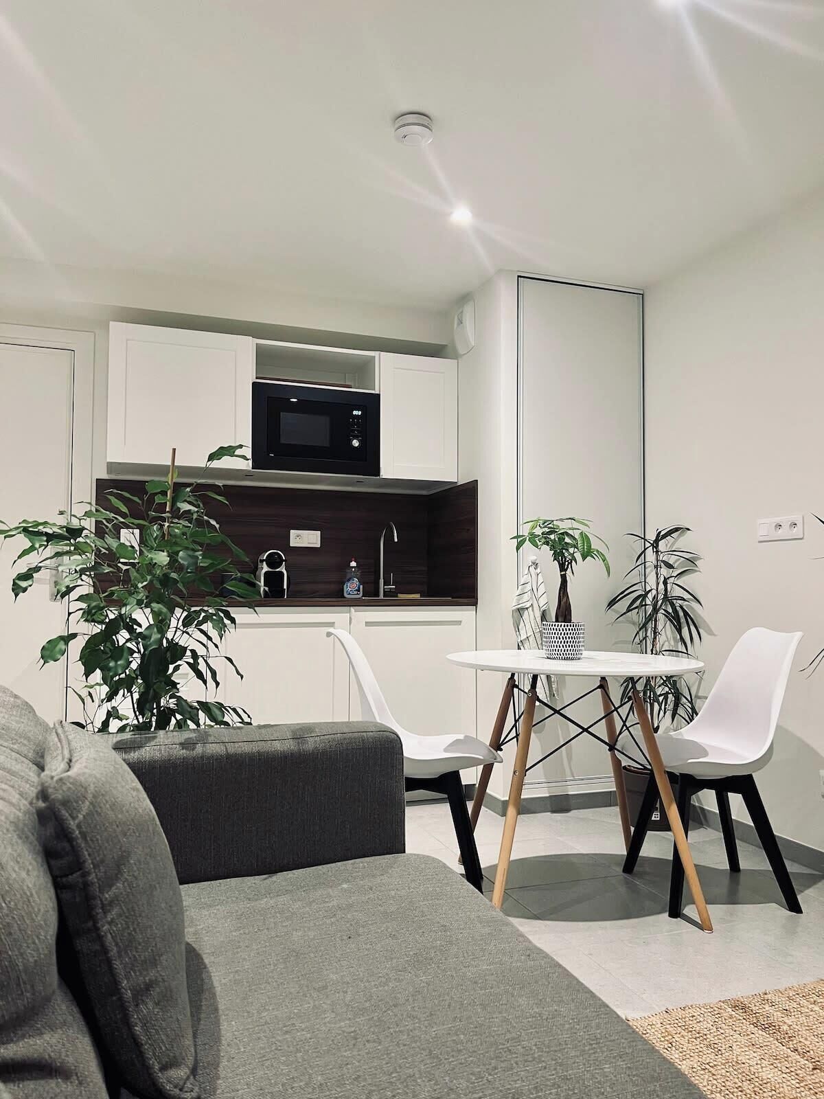 Een moderne keuken met witte kasten, een magnetron en een eethoek met een witte tafel en stoelen.