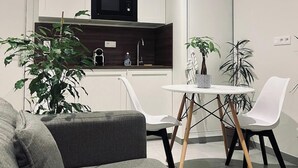 Moderni keittiö, jossa on valkoiset kaapit, mikroaaltouuni sekä ruokailutila, jossa on valkoinen pöytä ja tuolit.