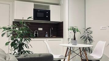 Een moderne keuken met witte kasten, een magnetron en een eethoek met een witte tafel en stoelen.