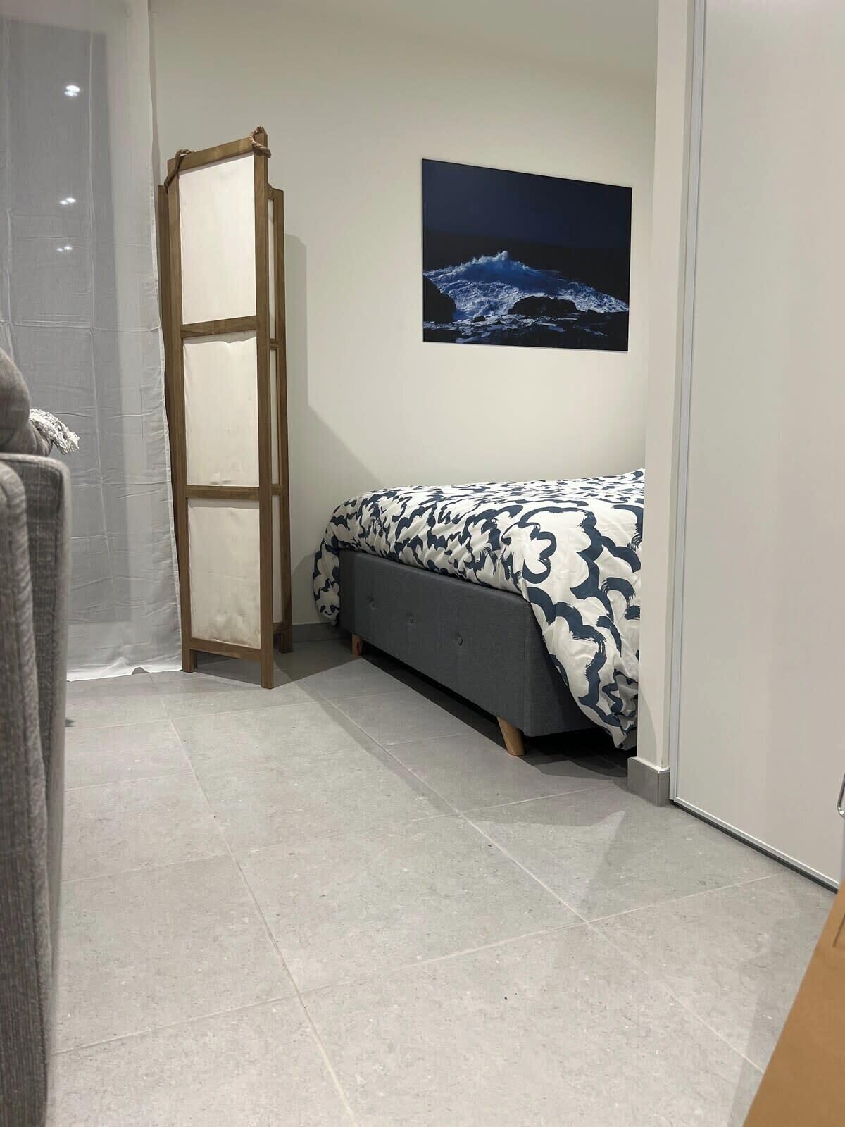 Une chambre à coucher avec un lit, une table de chevet, un tableau accroché au mur et une porte.