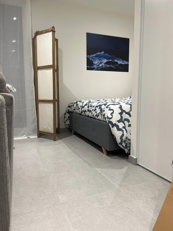 Un dormitorio con cama, mesita de noche, un cuadro en la pared y una puerta.