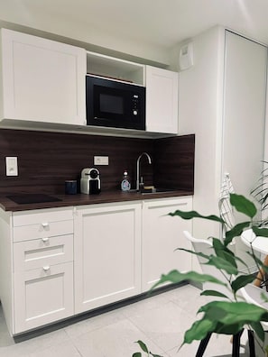 Una cocina moderna con armarios blancos, un microondas negro, una cafetera y un lavamanos.