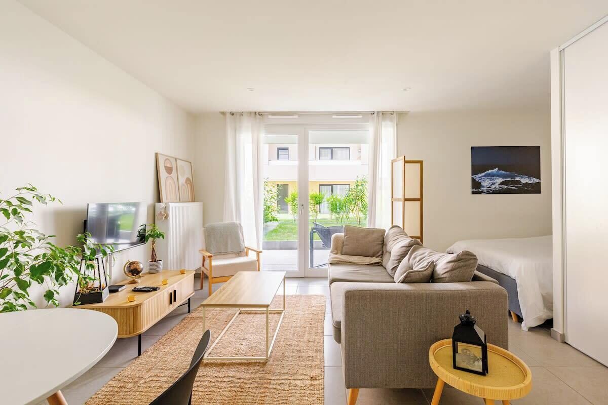 A modern hotel room with a sofa, a small table, a TV, and a view of the outdoors.